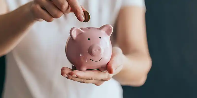 persona echando dinero a una hucha con forma de cerdito
